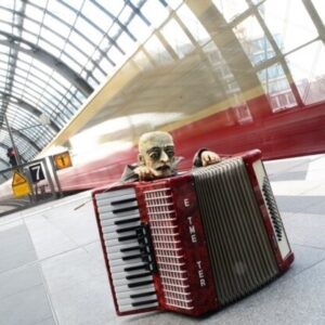 Puppe mit Akkordeon am Bahnsteig eines Bahnhofs