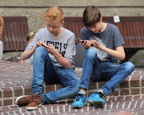 Zwei Jugendliche beschäftigen sich mit einem Handyspiel auf der Straße