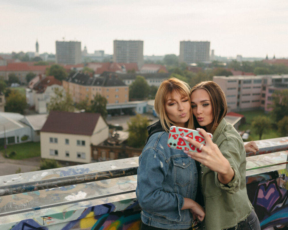 Auf dem Bild machen zwei Frauen ein gemeinsames Bild von sich auf dem Räucherturm Dessau. Im Hintergrund ist die Stadt zu sehen.