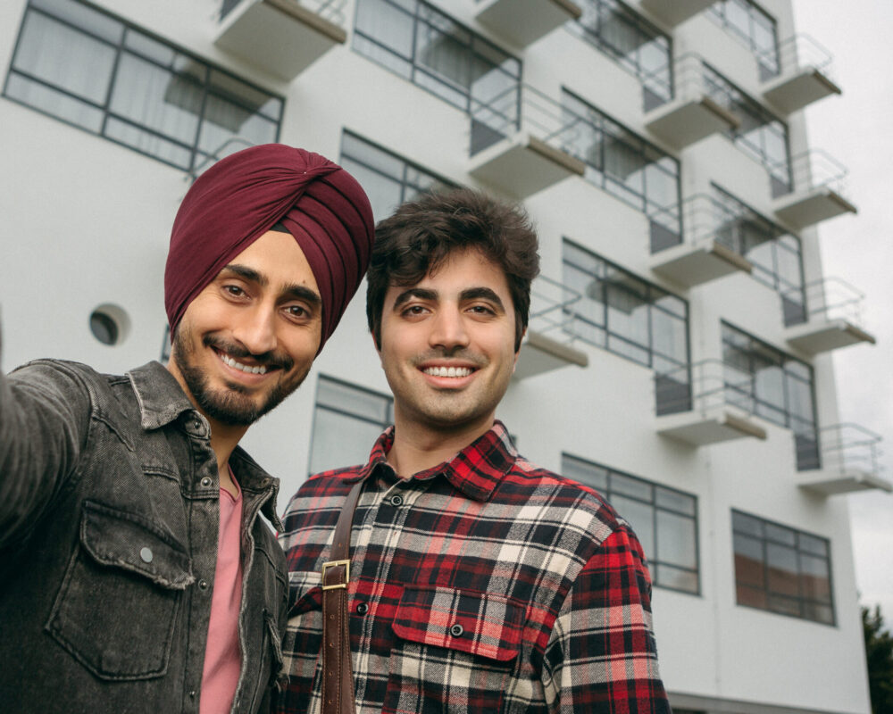 Auf dem Bild sind zwei junger Männer zu sehen, die ein Bild vor dem Bauhaus in Dessau machen. Einer der beiden trägt einen Turban. Das Bild wurde in der Selfie-Perspektive gemacht.