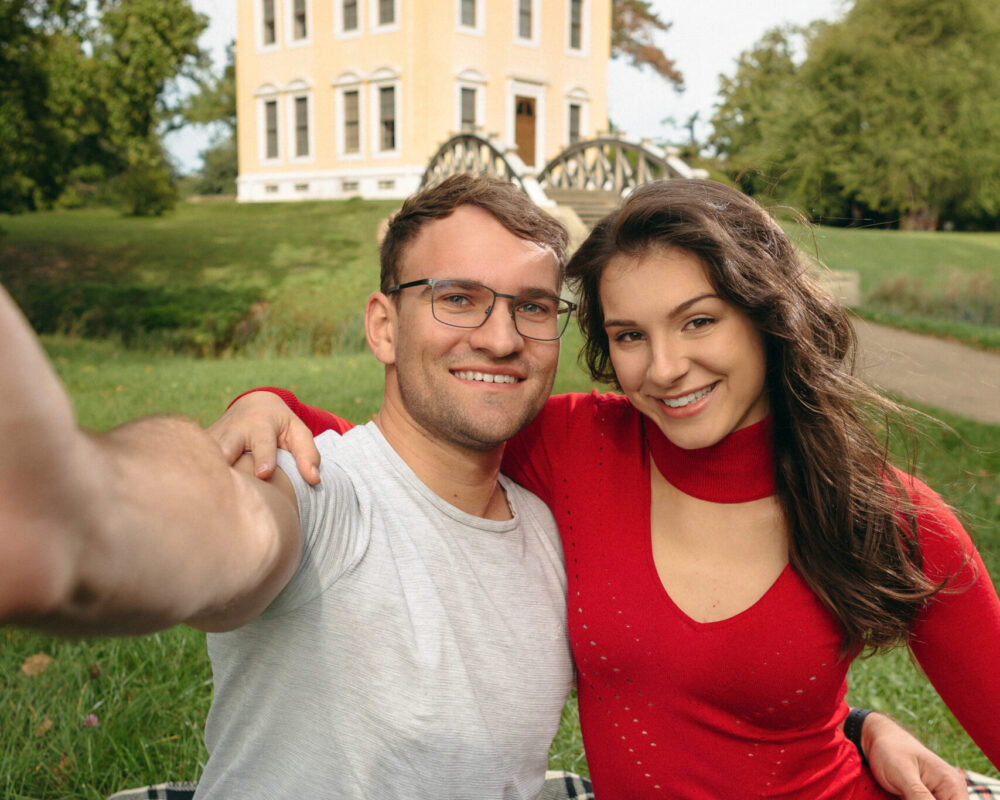 Ein junges Pärchen sitzt auf der Wiese und macht ein Selfie von sich un dem Luisium in Dessau