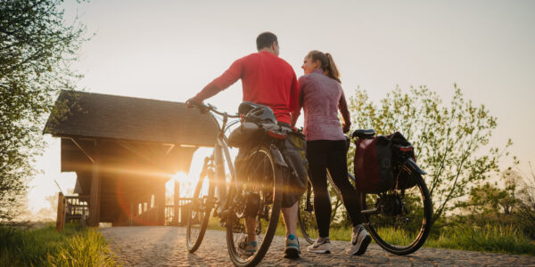 Pärchen schiebt ihre Räder beim Sonnenaufgang über eine Brücke